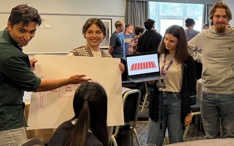 Groups of students in a room watching their peers present ideas on paper