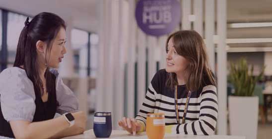 Two ladies sat at a table with a cup and chatting.